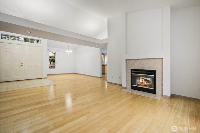 unfurnished living room with high vaulted ceiling, wood finished floors, baseboards, and a tile fireplace