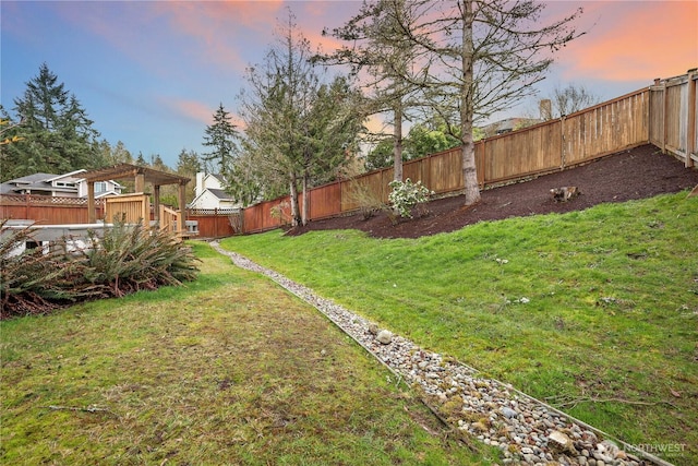 yard at dusk featuring a deck, a fenced backyard, and a pergola