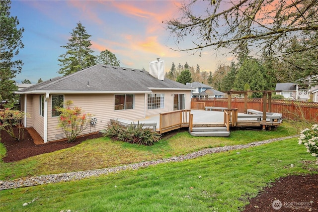 back of house with a shingled roof, fence, a wooden deck, a chimney, and a yard