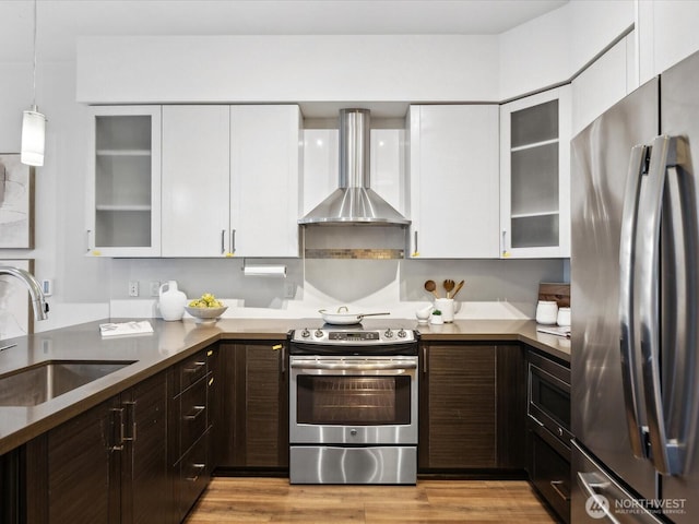 kitchen featuring a sink, appliances with stainless steel finishes, wall chimney range hood, and white cabinetry