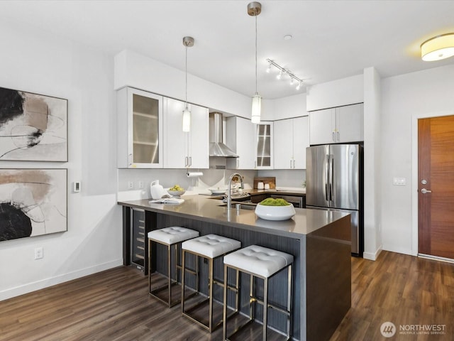 kitchen with a peninsula, wall chimney range hood, a kitchen bar, and freestanding refrigerator