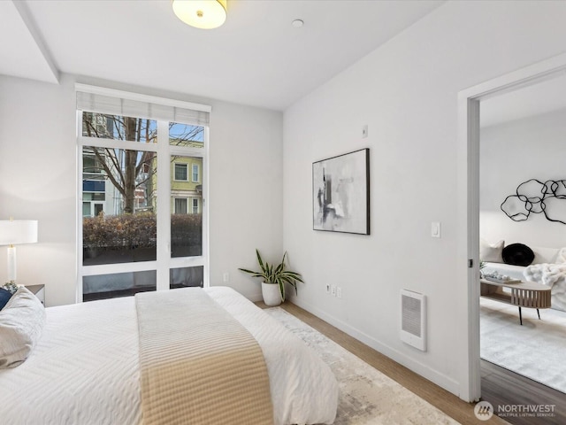 bedroom featuring heating unit, baseboards, and wood finished floors