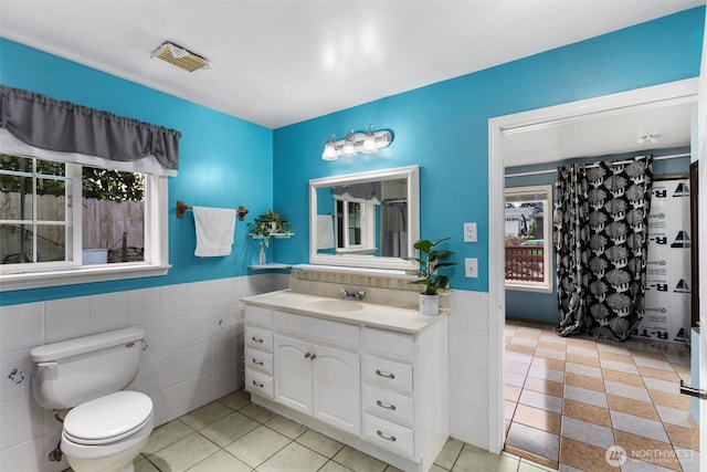 full bathroom featuring toilet, a wainscoted wall, vanity, visible vents, and tile walls