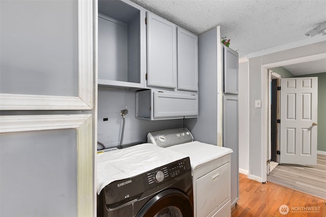 clothes washing area with a textured ceiling, baseboards, cabinet space, light wood finished floors, and washer and clothes dryer