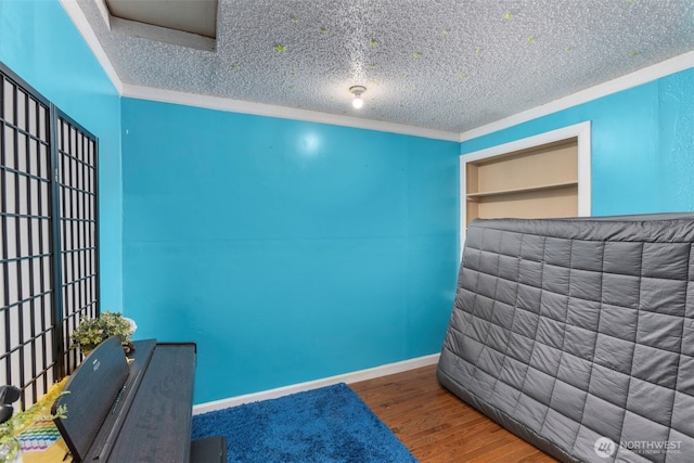 bedroom with a textured ceiling, baseboards, wood finished floors, and crown molding