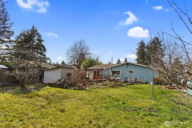 rear view of house with an outdoor structure, a lawn, a wooden deck, and fence