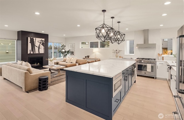 kitchen featuring open floor plan, stainless steel appliances, wall chimney exhaust hood, and light wood-style flooring