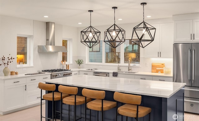 kitchen with light stone counters, stainless steel appliances, a kitchen island, a sink, and wall chimney range hood