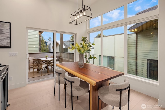 dining space with a towering ceiling, light wood-style flooring, baseboards, and a chandelier