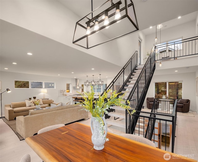 dining space featuring a towering ceiling, stairs, wood finished floors, and recessed lighting