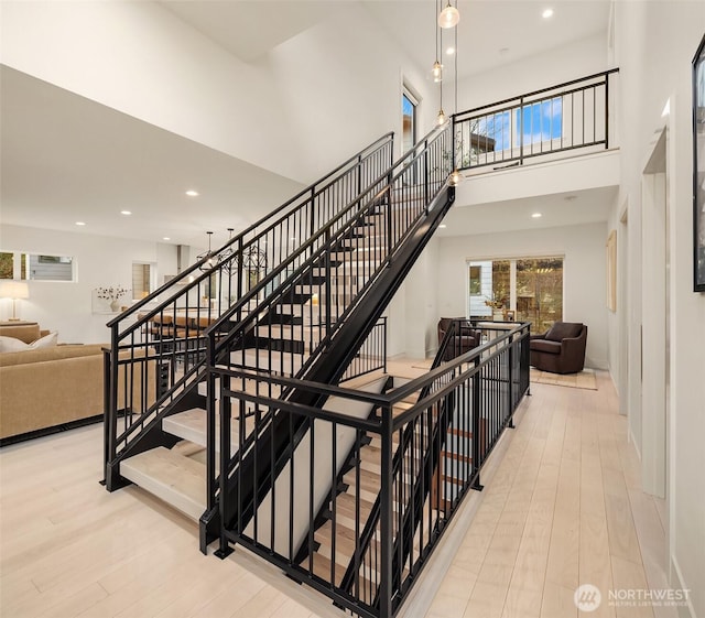 stairs featuring recessed lighting, a towering ceiling, and wood finished floors