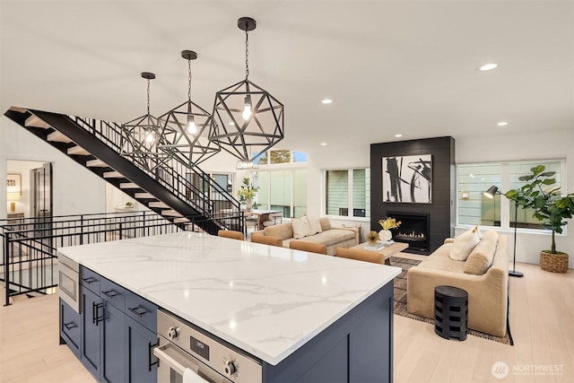 kitchen featuring light wood-style flooring, a large fireplace, stainless steel appliances, open floor plan, and a center island