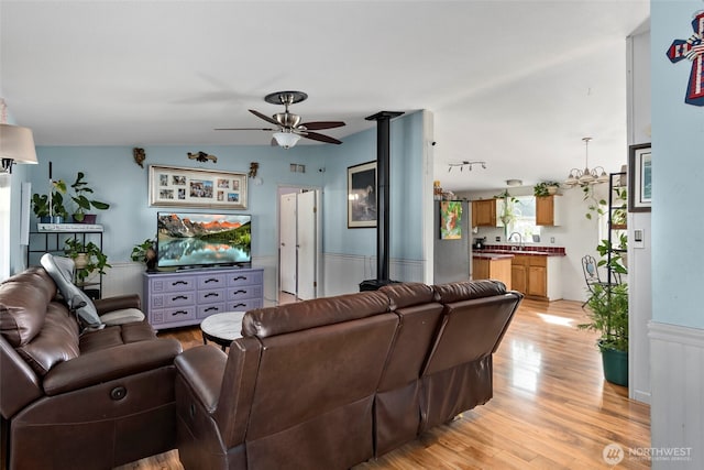 living room featuring light wood-type flooring, ceiling fan with notable chandelier, vaulted ceiling, and wainscoting