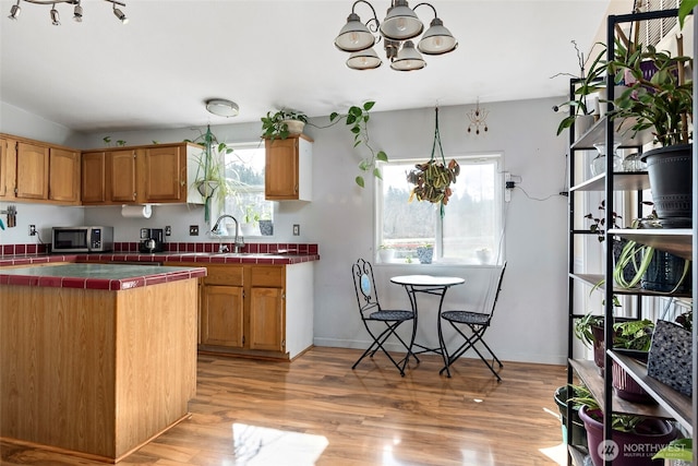 kitchen featuring tile countertops, a sink, light wood-type flooring, stainless steel microwave, and an inviting chandelier