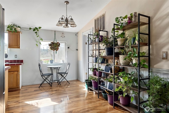 dining area featuring light wood-type flooring, an inviting chandelier, baseboards, and vaulted ceiling