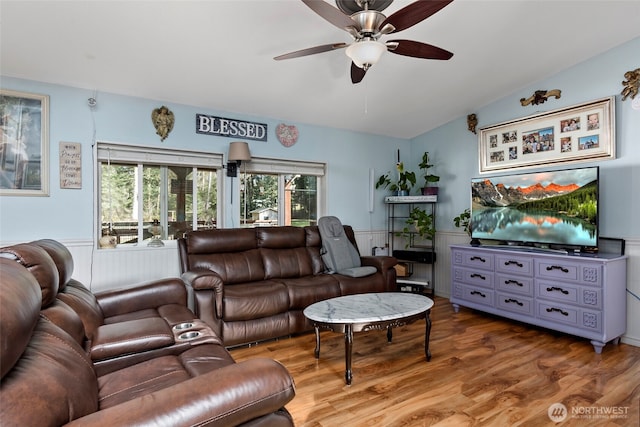 living area featuring lofted ceiling, a wainscoted wall, ceiling fan, and wood finished floors