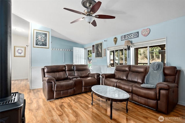 living area with a wood stove, light wood-style floors, ceiling fan, and lofted ceiling