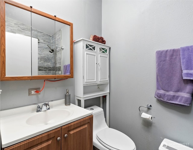 bathroom featuring tiled shower, vanity, and toilet