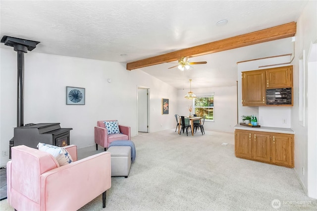 living room with lofted ceiling with beams, a textured ceiling, light carpet, a ceiling fan, and a wood stove