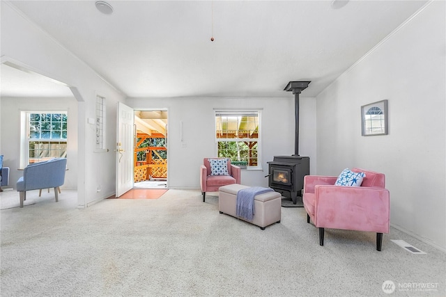 living area featuring arched walkways, visible vents, carpet, and a wood stove