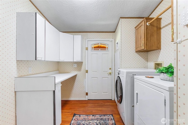 laundry area with wallpapered walls, cabinet space, washing machine and clothes dryer, a textured ceiling, and light wood-type flooring