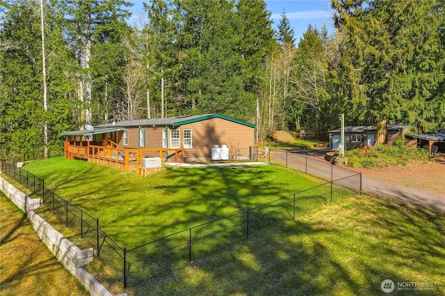 view of front of property with a fenced backyard, dirt driveway, a wooden deck, a forest view, and a front lawn