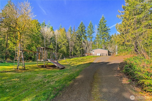 exterior space with dirt driveway, playground community, and a view of trees