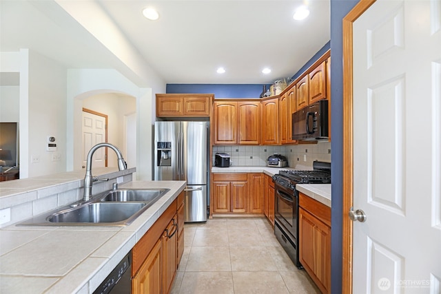 kitchen with light tile patterned floors, tile counters, tasteful backsplash, a sink, and black appliances