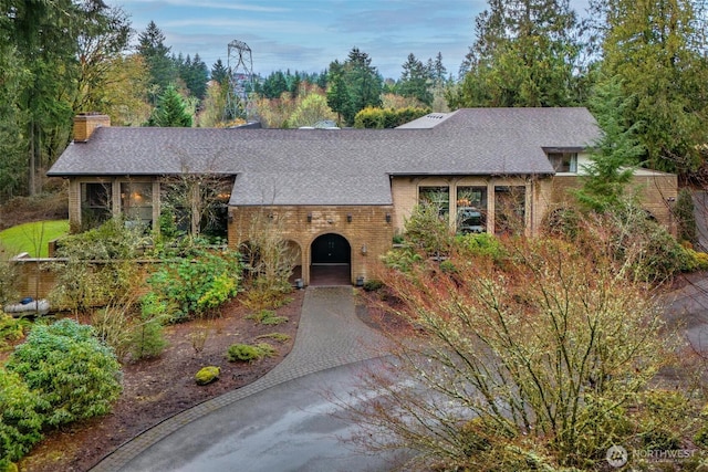 view of front of property with a shingled roof, decorative driveway, brick siding, and a chimney