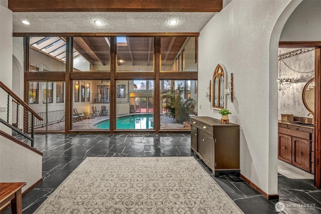 doorway with arched walkways, beam ceiling, stone tile flooring, a textured wall, and baseboards