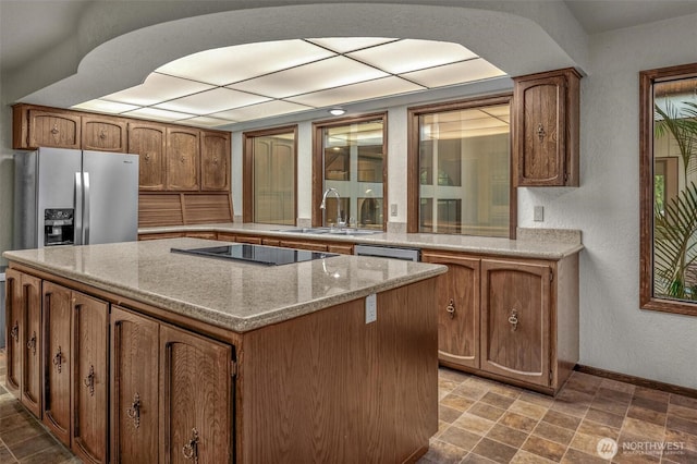 kitchen with a sink, black electric stovetop, brown cabinetry, and a kitchen island