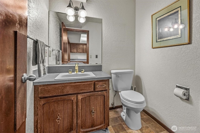 half bath with a textured wall, vanity, toilet, and baseboards