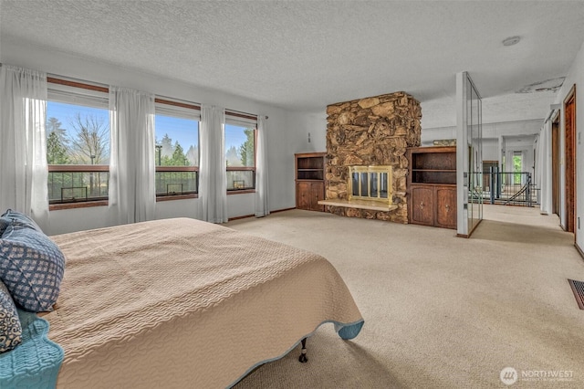 bedroom featuring a textured ceiling, a stone fireplace, carpet, and visible vents