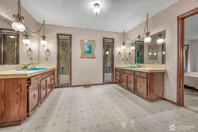 bathroom with wallpapered walls, a sink, a textured ceiling, and tile patterned floors