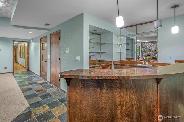 bar featuring a sink, visible vents, baseboards, hanging light fixtures, and stone finish flooring