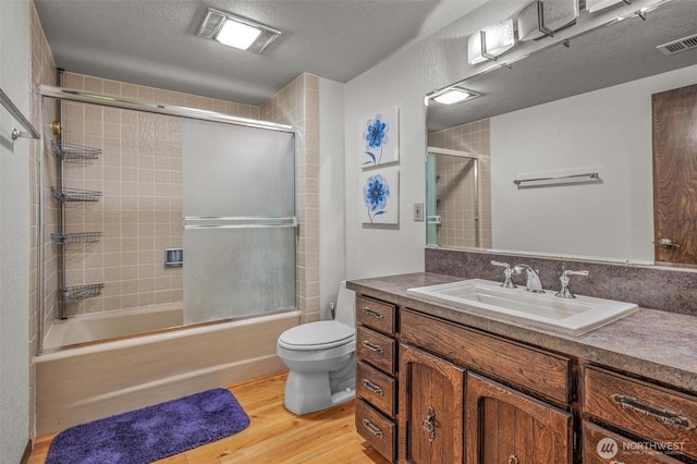 bathroom featuring toilet, wood finished floors, vanity, visible vents, and combined bath / shower with glass door