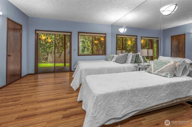 bedroom featuring access to outside, a textured ceiling, baseboards, and wood finished floors