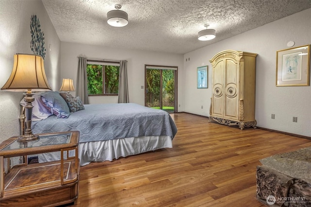 bedroom featuring access to outside, a textured ceiling, baseboards, and wood finished floors