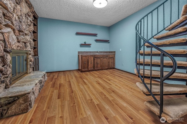 bar with a textured ceiling, a stone fireplace, baseboards, light wood-style floors, and stairway