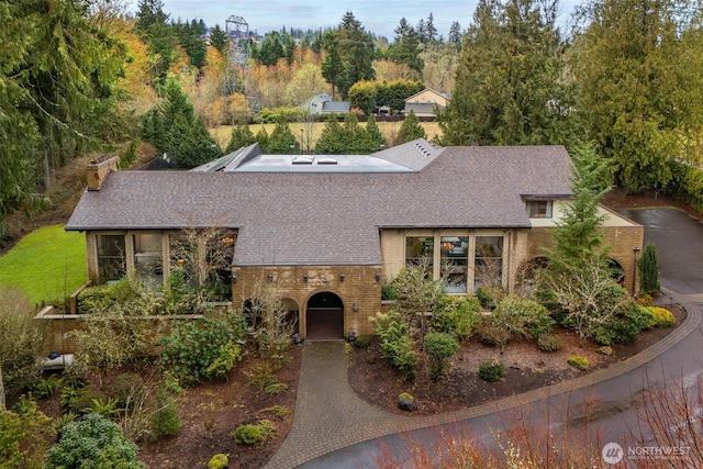 view of front facade with decorative driveway, brick siding, and roof with shingles