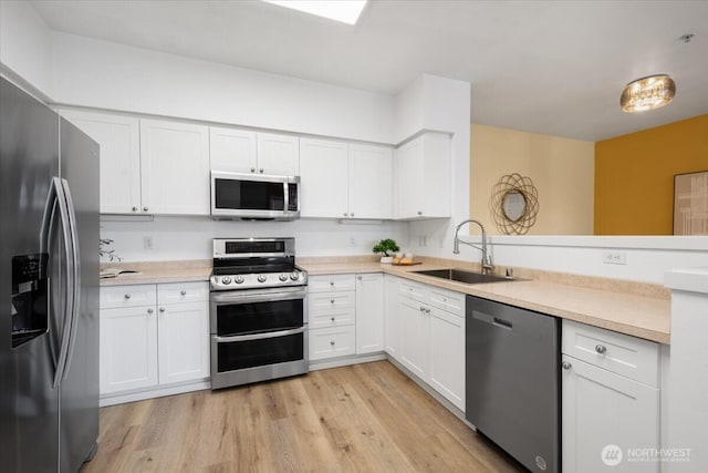 kitchen featuring stainless steel appliances, light countertops, light wood-style floors, white cabinets, and a sink