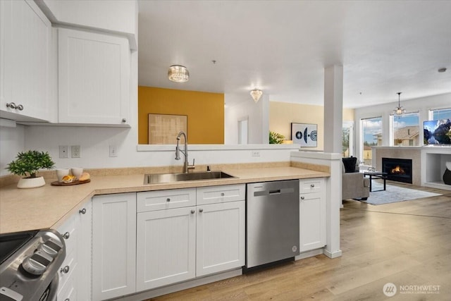 kitchen with stainless steel appliances, open floor plan, white cabinetry, a sink, and a lit fireplace