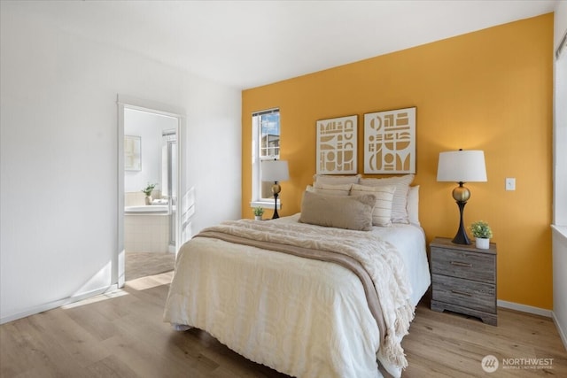 bedroom with ensuite bathroom, baseboards, and wood finished floors