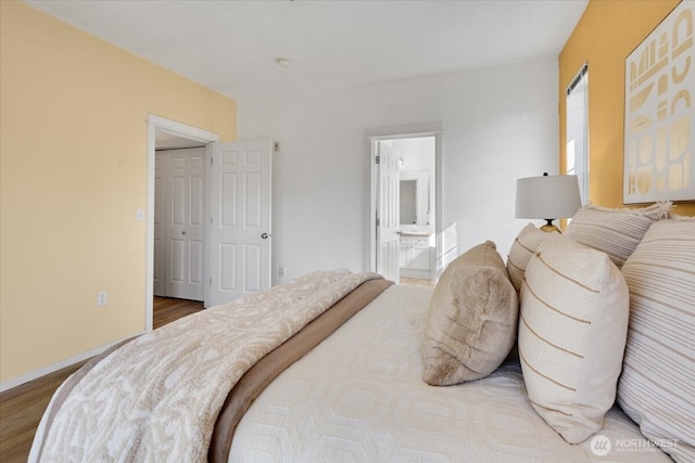 bedroom with ensuite bath, baseboards, and wood finished floors