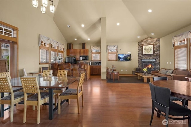 dining room featuring high vaulted ceiling, a stone fireplace, dark wood-type flooring, and recessed lighting