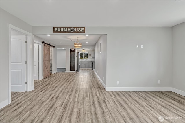unfurnished living room with a barn door, light wood-style floors, and baseboards