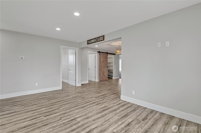 empty room with a barn door, recessed lighting, wood finished floors, and baseboards