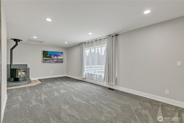 unfurnished living room with carpet, recessed lighting, visible vents, a wood stove, and baseboards