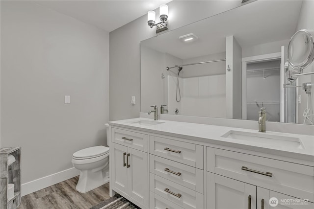 full bath featuring toilet, double vanity, a sink, and wood finished floors