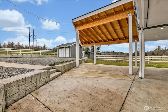 view of patio with a rural view, fence, a storage unit, and an outdoor structure